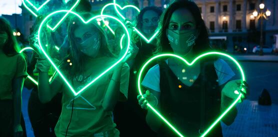 Das Bild zeigt mehrere Frauen, die grüne Neonherzen in der Hand halten