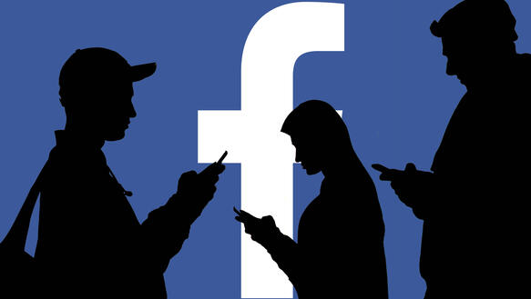 Das Bild zeigt eine Illustration: Die Silhouette mehrere Menschen mit Handy vor einem blauen Facebook-Hintergrund